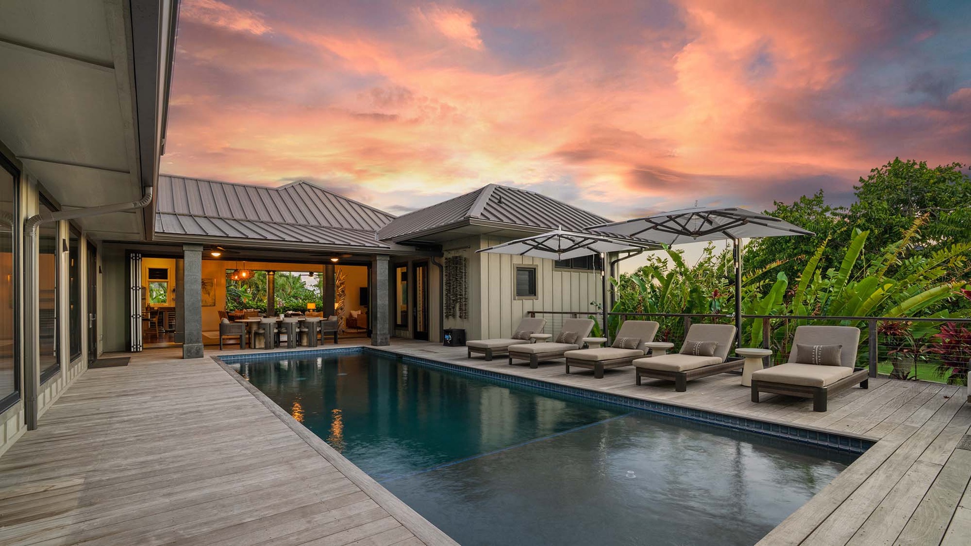 A stunning sunset paints the sky over this tropical retreat, featuring a pristine pool and private deck surrounded by lush greenery—perfect for relaxation and outdoor living.