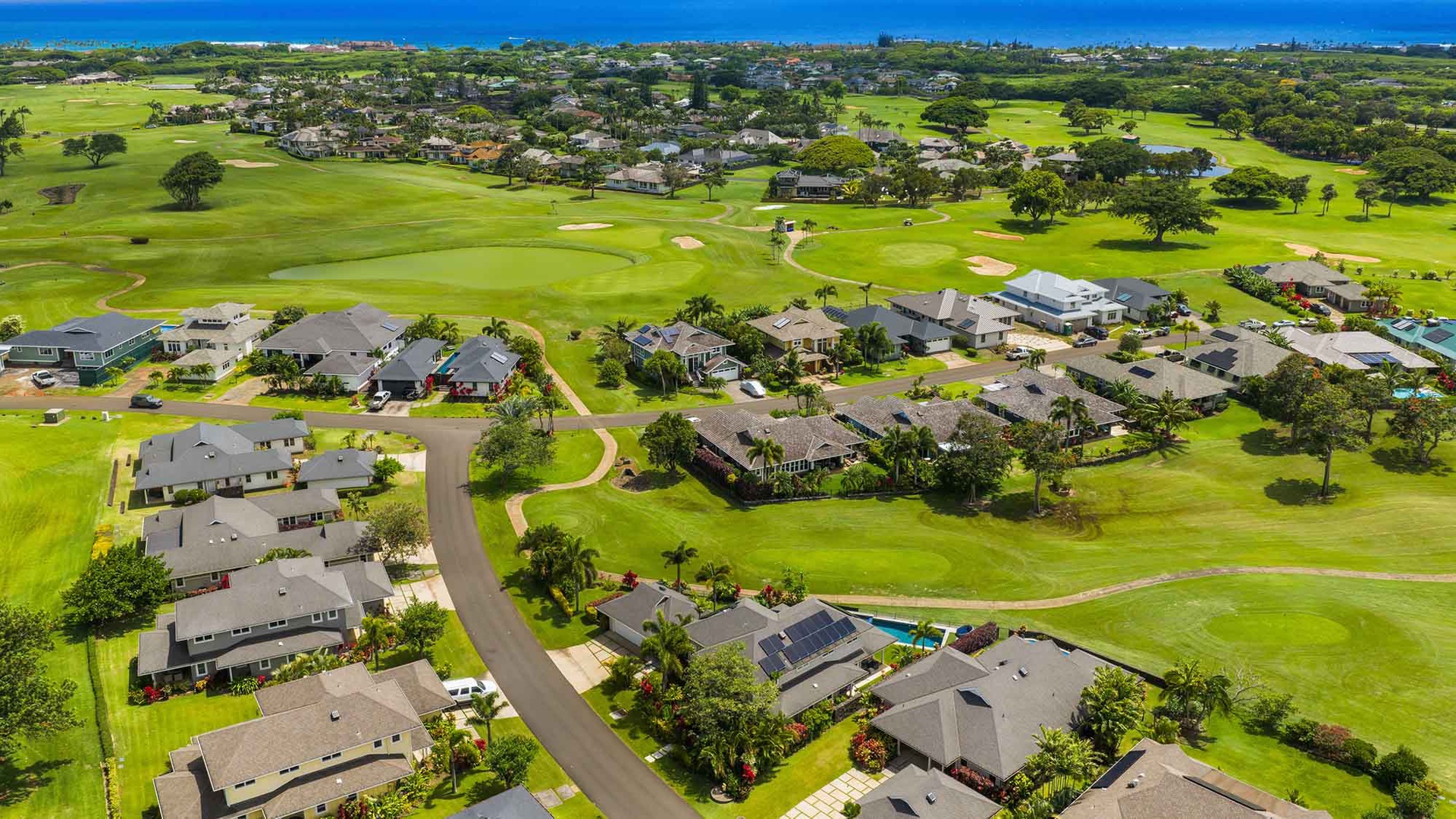 Aerial view of a residential community nestled within a championship golf course, with pristine fairways and ocean views in the distance.