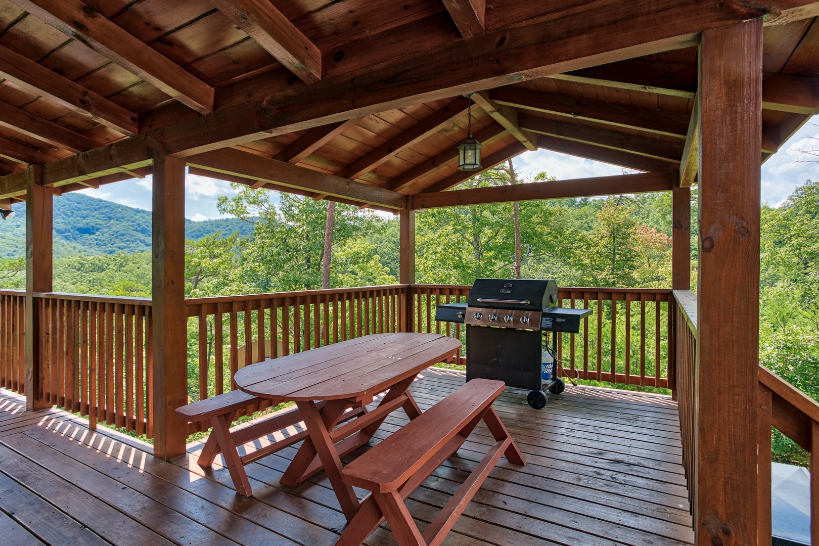 A propane grill and picnic table on the covered deck at Four Seasons Lodge, a 3-bedroom cabin rental located in Pigeon Forge