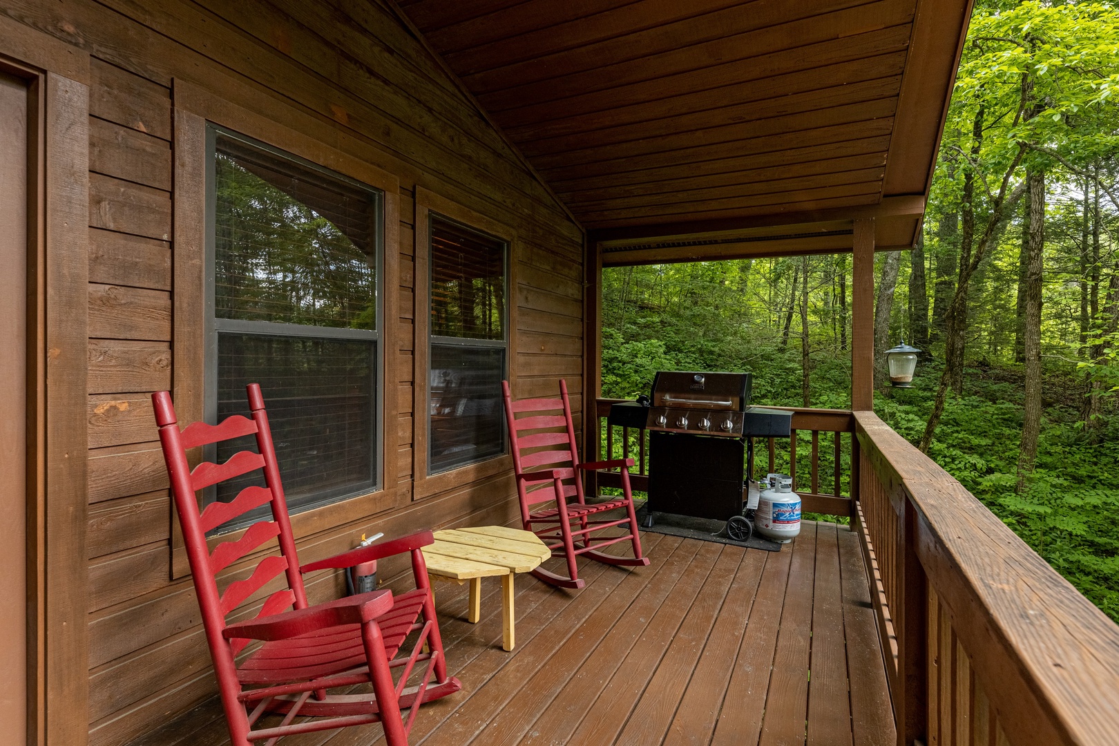 Rocking chairs and a grill on a covered porch at Hawk's Heart Lodge, a 3 bedroom cabin rental located in Pigeon Forge