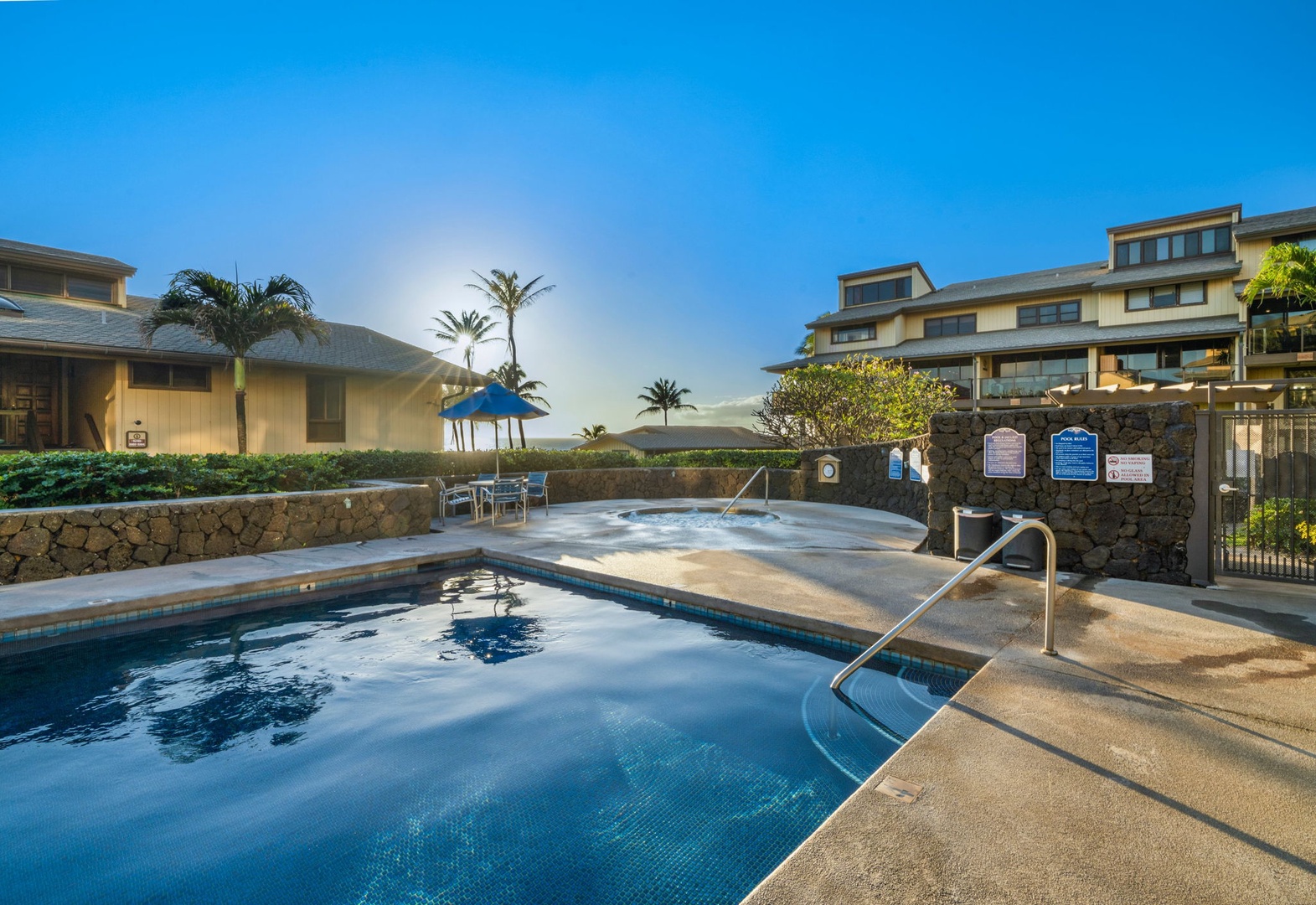 A tropical resort complex featuring a pool and hot tub area surrounded by lush landscaping and multi-level residential buildings under a clear Hawaiian sky.