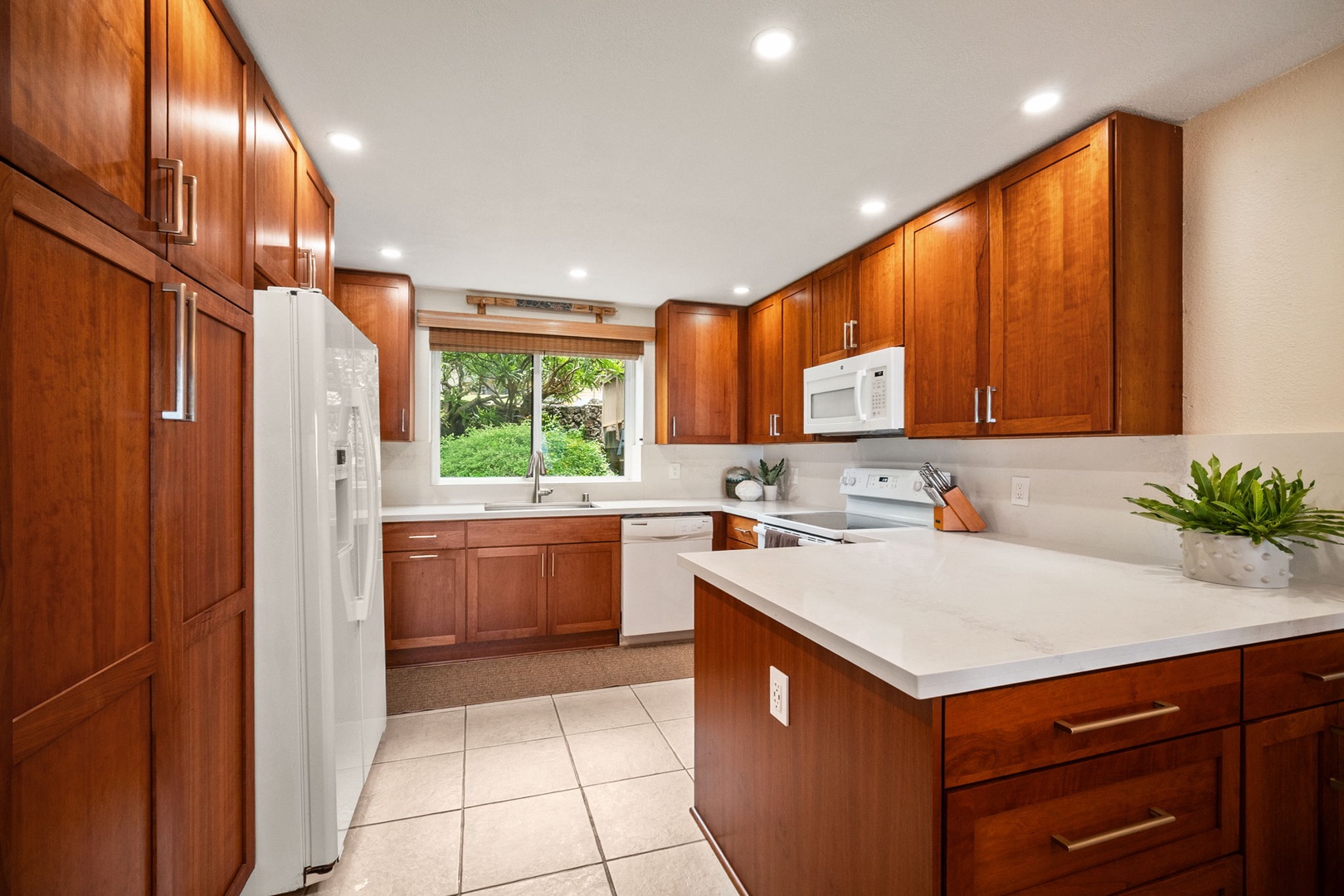 Picture yourself preparing meals in this bright, fully equipped kitchen with gleaming counters, warm wood cabinetry, and garden views framing your cooking time.