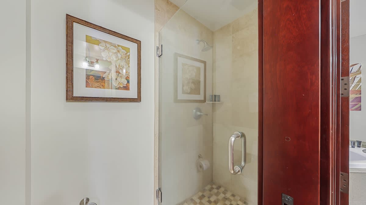 Your private bathroom features a spacious walk-in shower with elegant stone tiling, warm lighting, and thoughtful artwork that makes every morning feel like a spa retreat.
