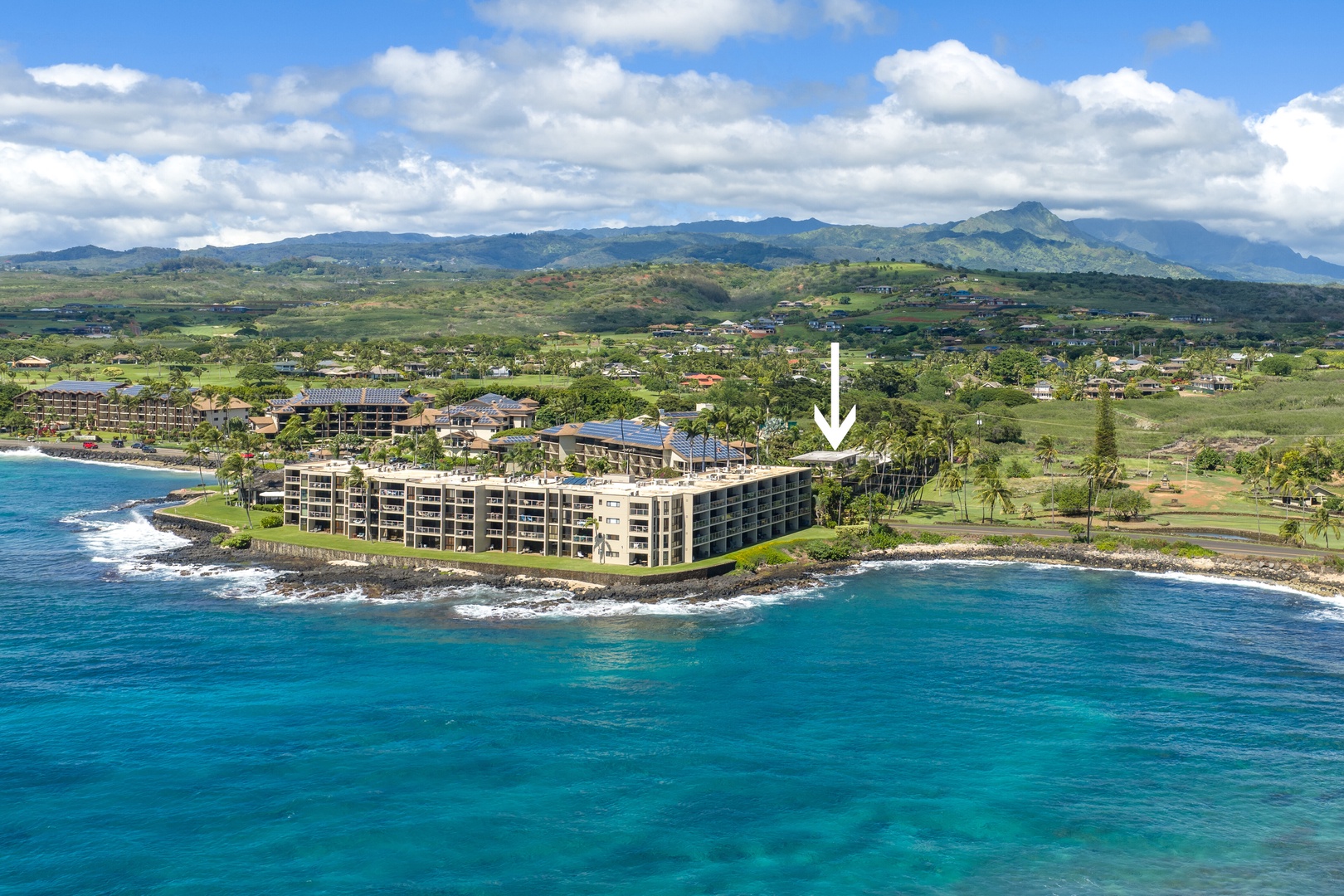 Oceanfront resort building positioned along pristine coastline with mountains rising beyond green rolling landscape.