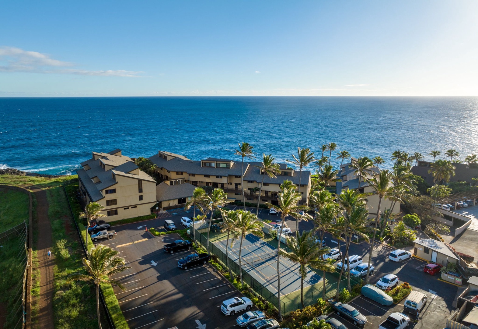 Oceanfront property featuring tennis courts, parking, and tropical landscaping with direct beach access and stunning coastal views.