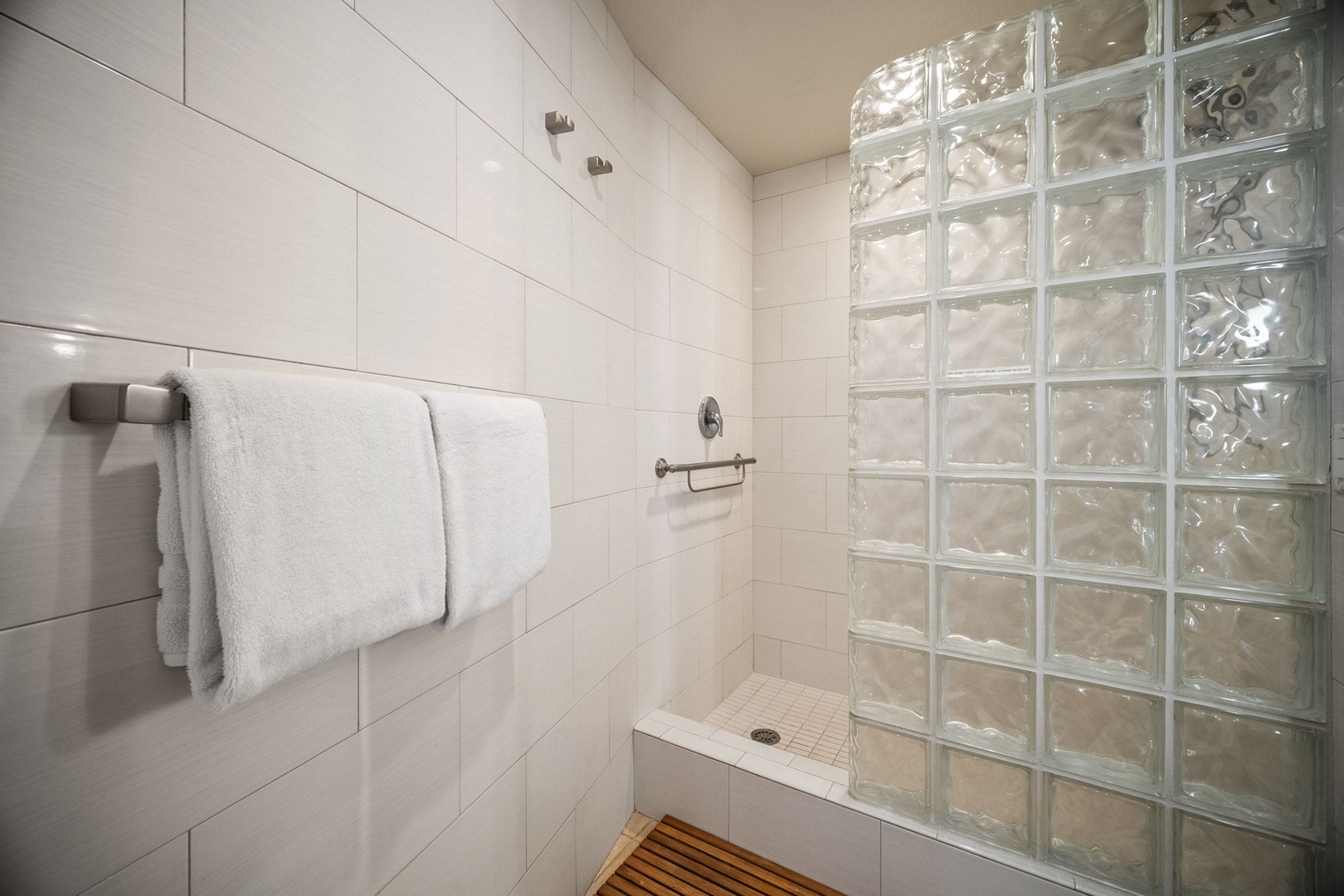 Step into your private shower with elegant glass block details and fresh, fluffy towels waiting for you. The clean white tile and thoughtful design create a spa-like retreat.