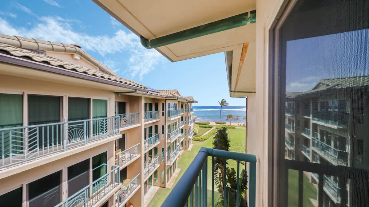 The property is nestled in a beachfront location with lush landscaped grounds and ocean views just beyond the palm trees and green lawn.