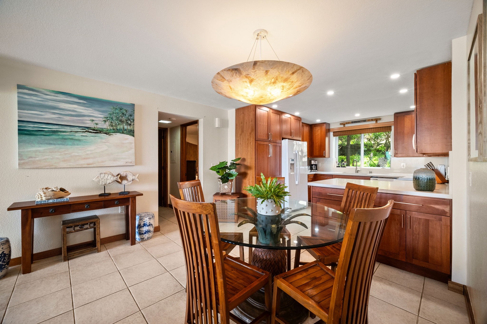 Gather around the glass-top dining table in your open-concept kitchen, where warm wood cabinetry, stainless steel appliances, and natural light create the perfect space for memorable meals together.