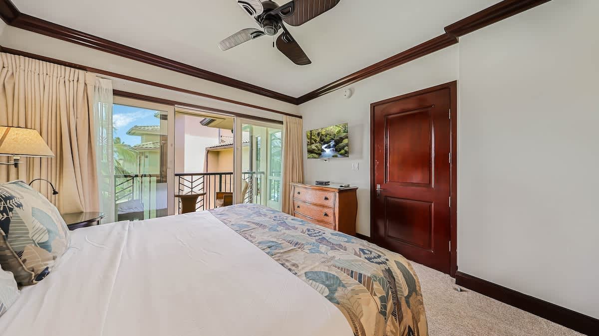 Sink into your plush bed beneath a tropical ceiling fan, with sliding doors opening to your private balcony and lush green views. Rich wood tones and soft lighting create a peaceful retreat.