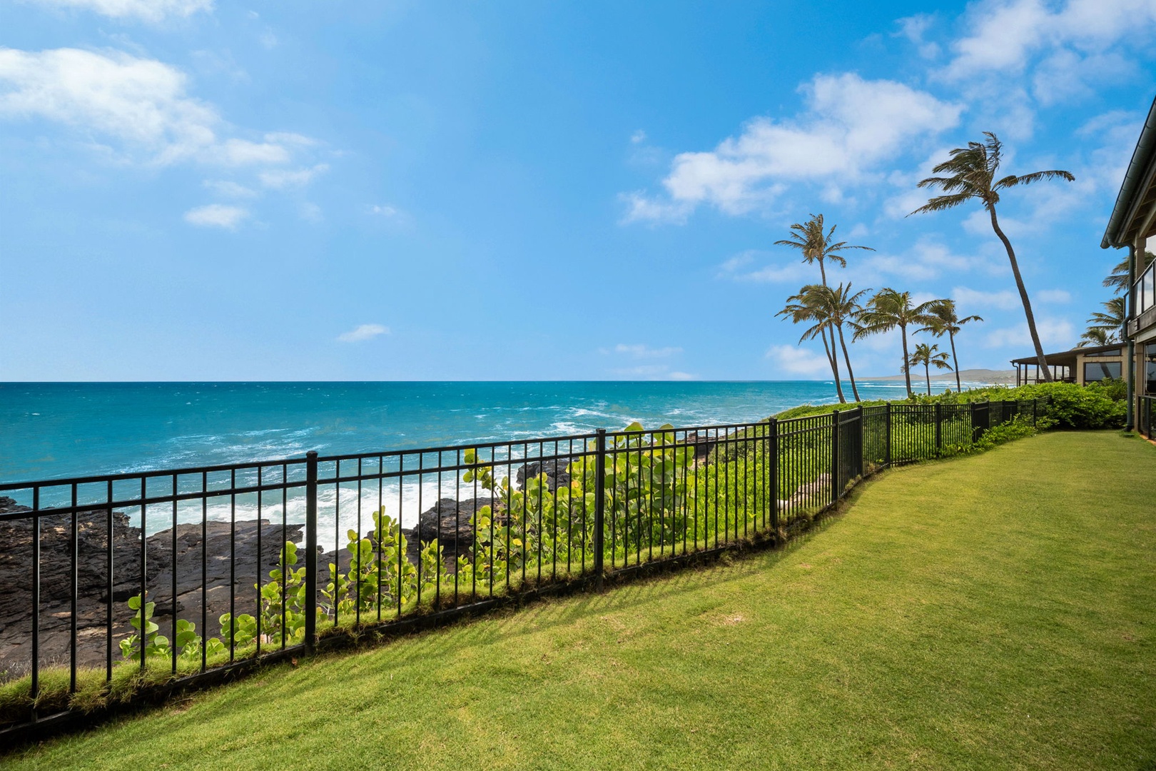 This oceanfront property features sweeping sea views, lush green lawn, swaying palms, and rocky shoreline, framing a tranquil tropical escape in a pristine coastal setting.