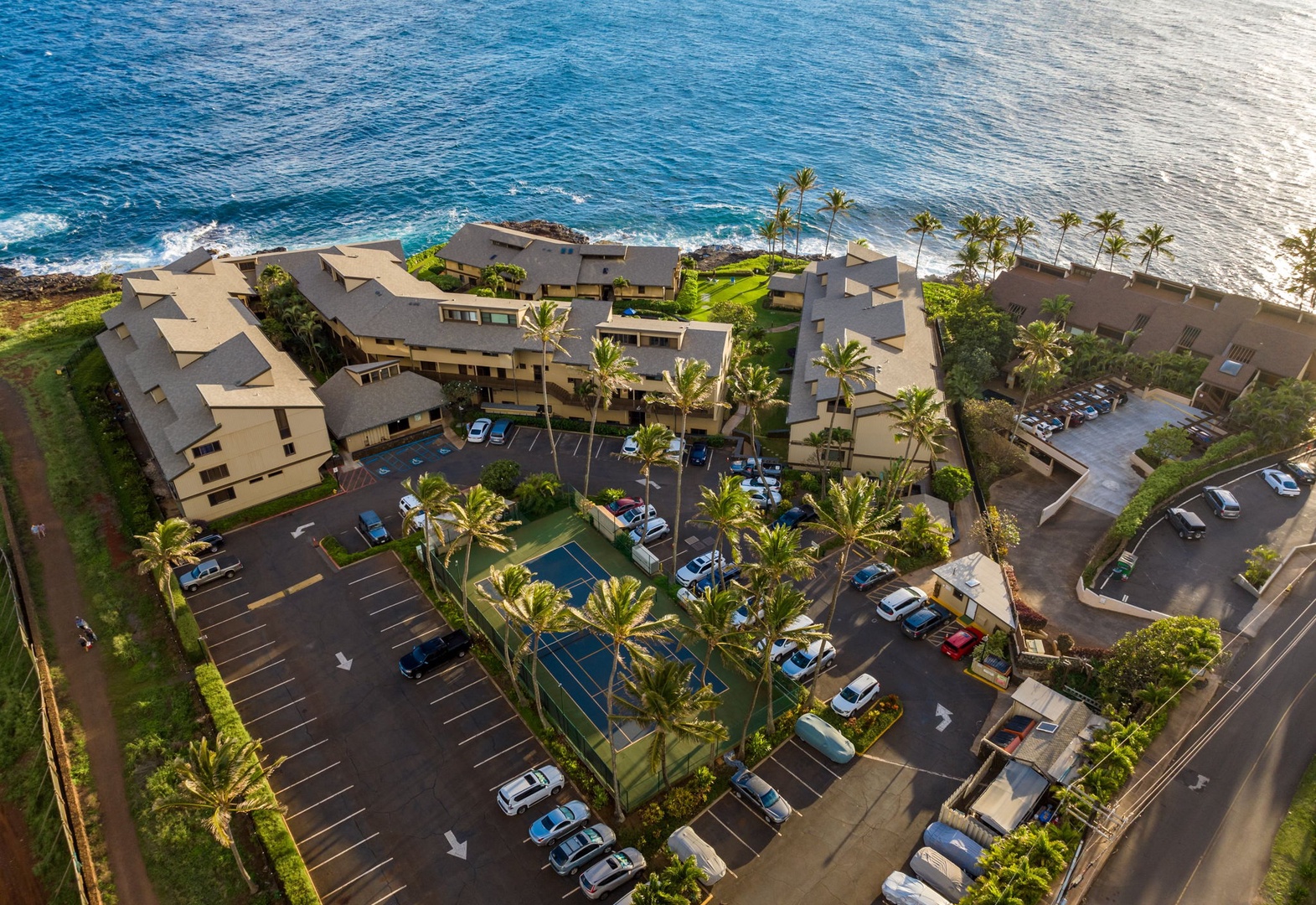 Aerial view of an oceanfront vacation rental property featuring lush tropical landscaping, tennis court, swimming pool, and direct beach access along pristine blue waters.