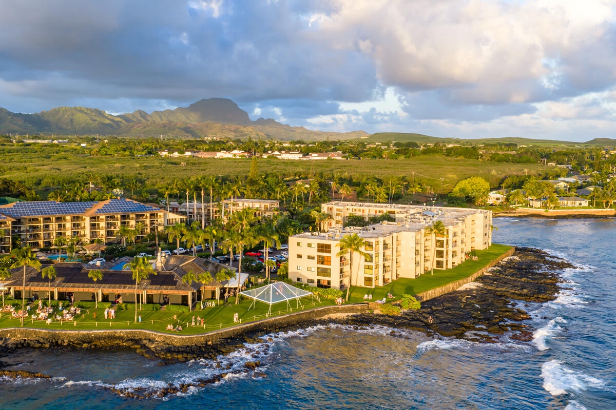 Oceanfront resort buildings nestled along volcanic coastline with dramatic mountain backdrop and lush tropical landscape.