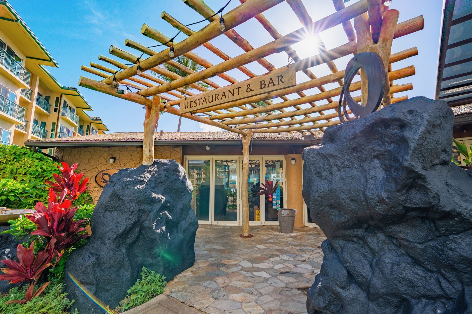 The property's restaurant and bar entrance features tropical landscaping and a covered patio area, located within the resort complex.