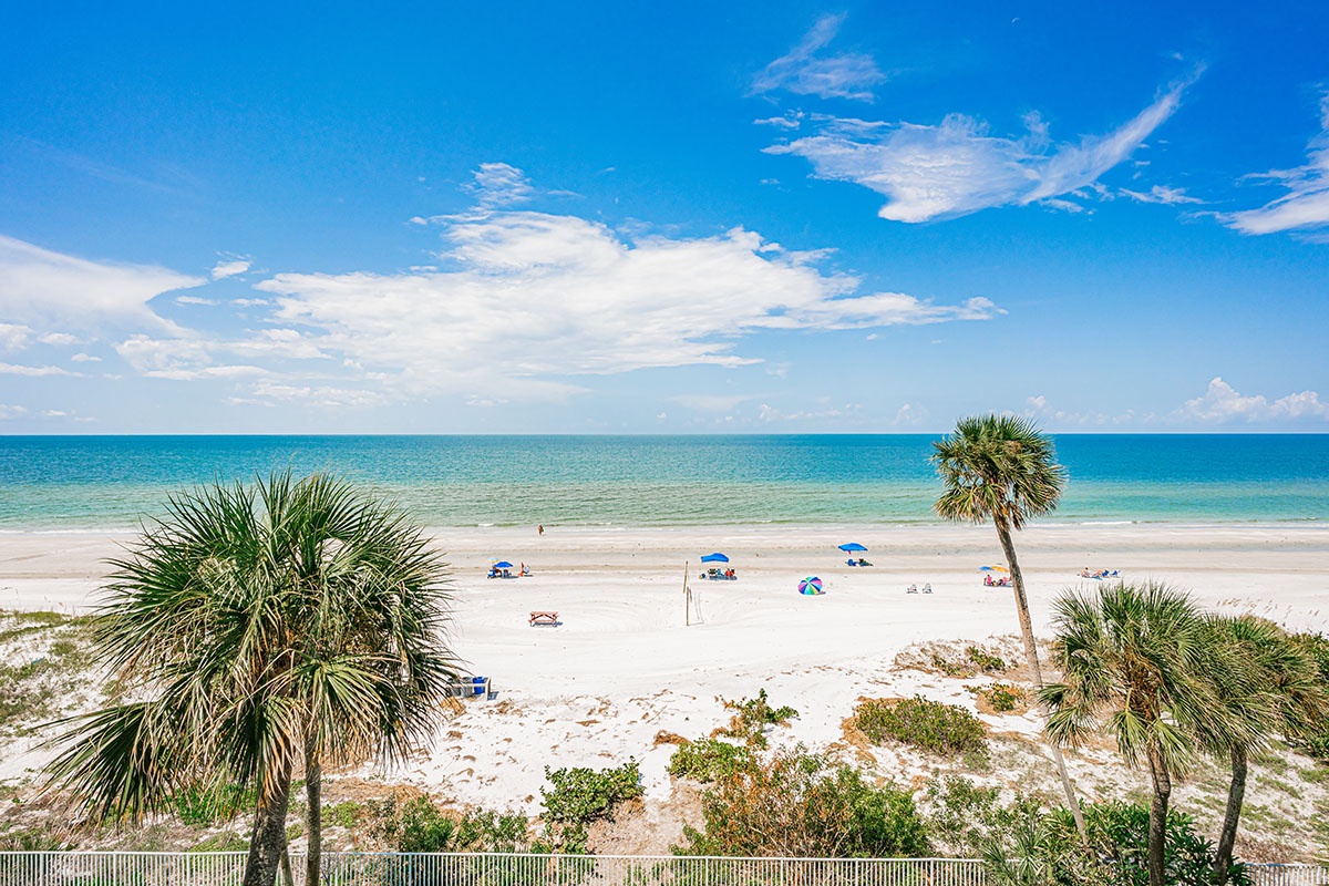 Pristine beach with white sand and turquoise waters surrounded by swaying palm trees under brilliant blue skies.