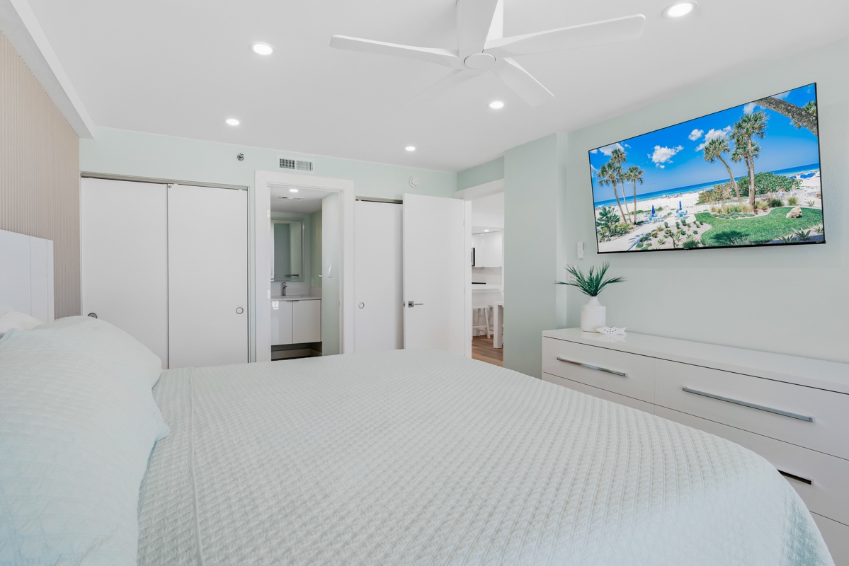 Unwind in your serene bedroom sanctuary with crisp linens, calming coastal hues, and tropical vibes on the wall-mounted TV.