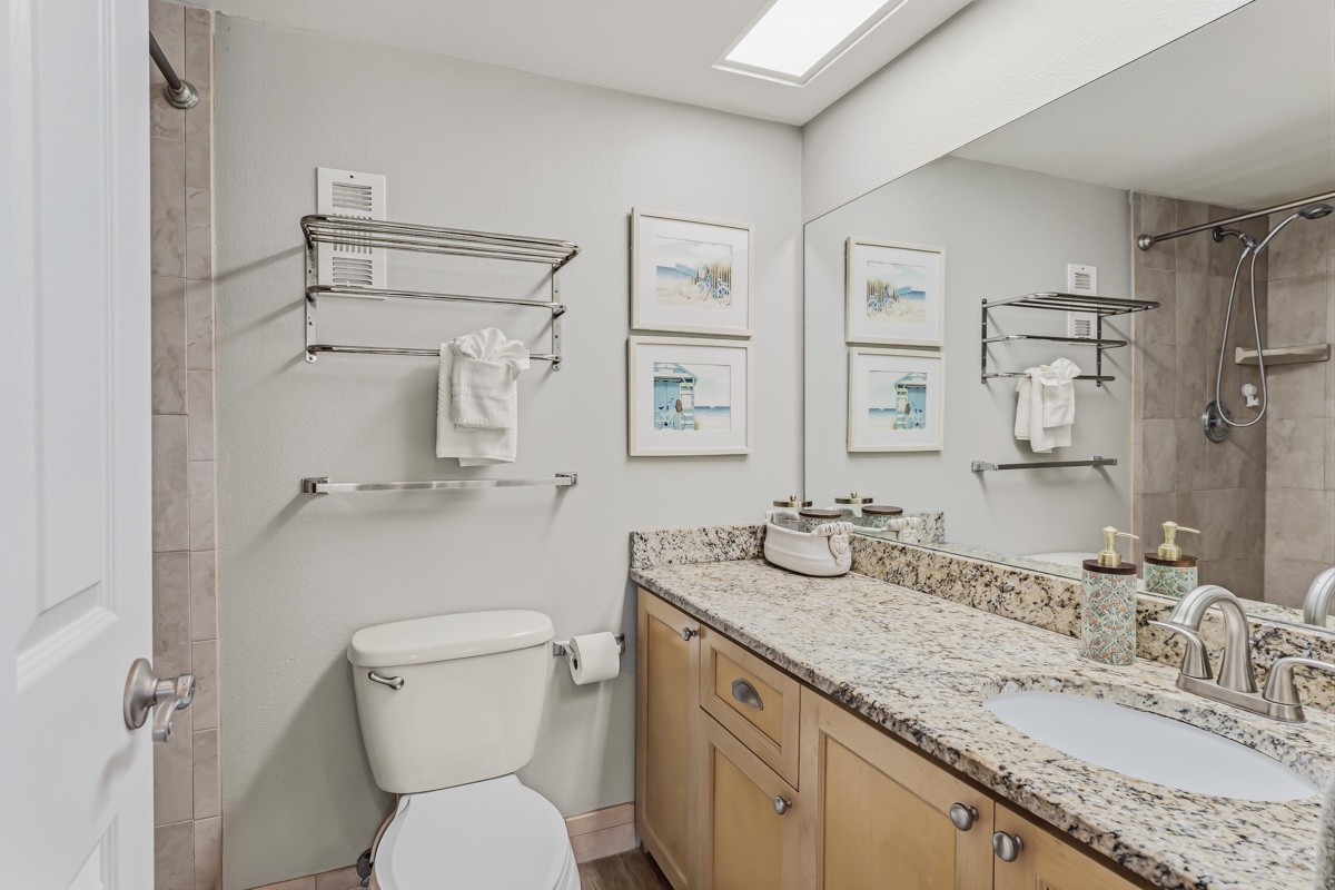 Step into your bright, modern bathroom with coastal charm—plush towels await, skylight floods the space with natural light, and granite countertops add elegance to your morning routine.