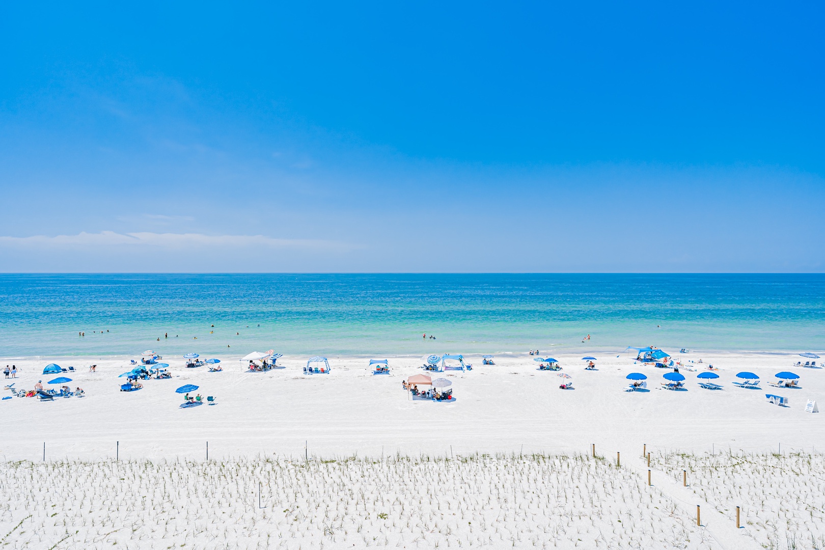 White sand stretches toward clear turquoise waters beneath endless blue skies. Spend your days relaxing under an umbrella or wading into the gentle waves, surrounded by pure coastal beauty.