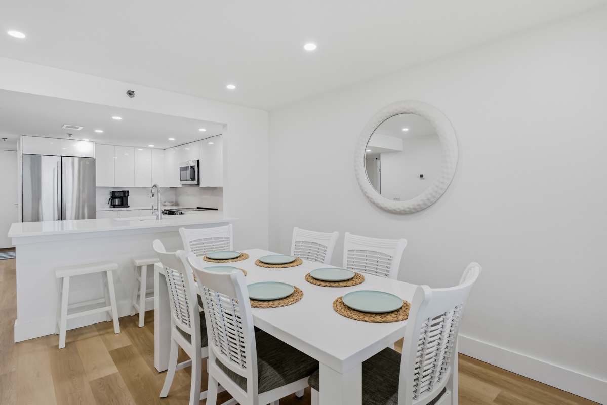 Your modern dining space flows seamlessly into a fully equipped kitchen, where coastal-inspired touches and clean white finishes create the perfect setting for memorable meals.