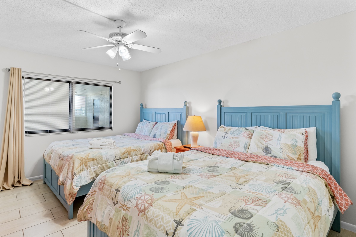 Rest comfortably in your coastal bedroom with two cozy beds, crisp linens, and gentle ceiling fan breezes creating the perfect sleep sanctuary.