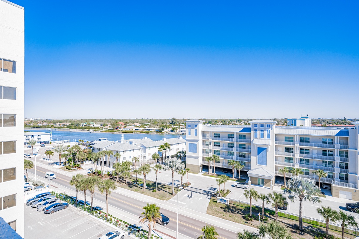 Coastal cityscape with modern buildings, palm-lined streets, and waterfront views under clear blue skies.