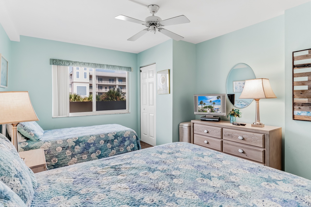 Relax in your tranquil bedroom with soft coastal colors and comfortable twin beds. A ceiling fan keeps you cool while natural light fills the space through the window.