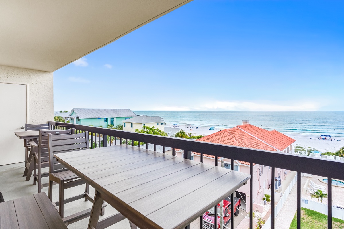 Expansive balcony overlooks vibrant beachfront homes and sparkling Gulf waters stretching to the horizon under bright blue skies.