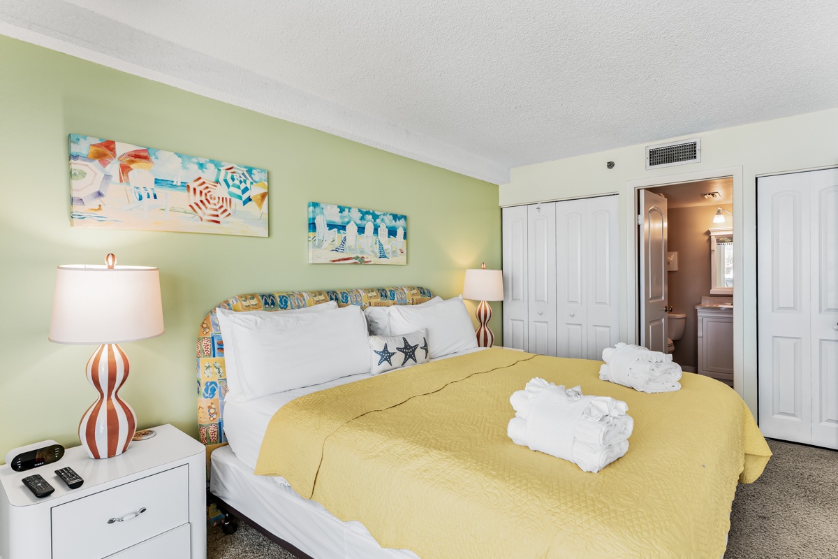 Step into your cheerful bedroom retreat, where soft green walls and coastal artwork set a relaxed, beachy vibe. Crisp white linens and fluffy towels await you after a day of exploring.