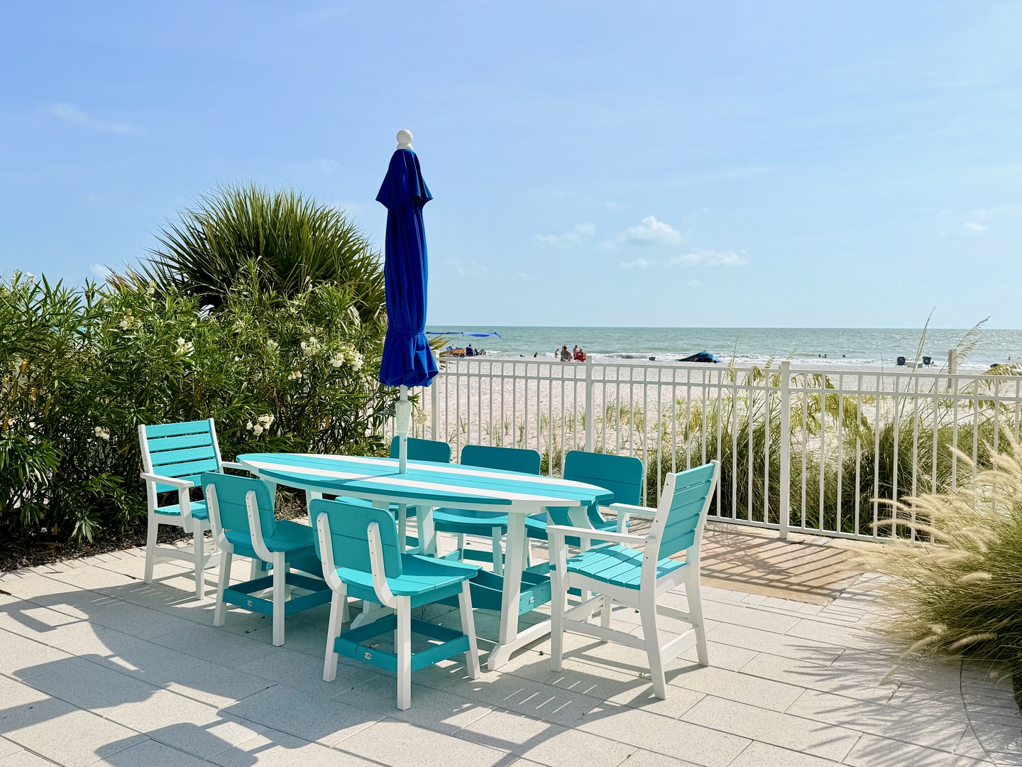 Step out to your private patio and feel the coastal breeze. Bright turquoise seating invites morning coffee or sunset dinners, just steps from the sandy shore beyond the white railing.