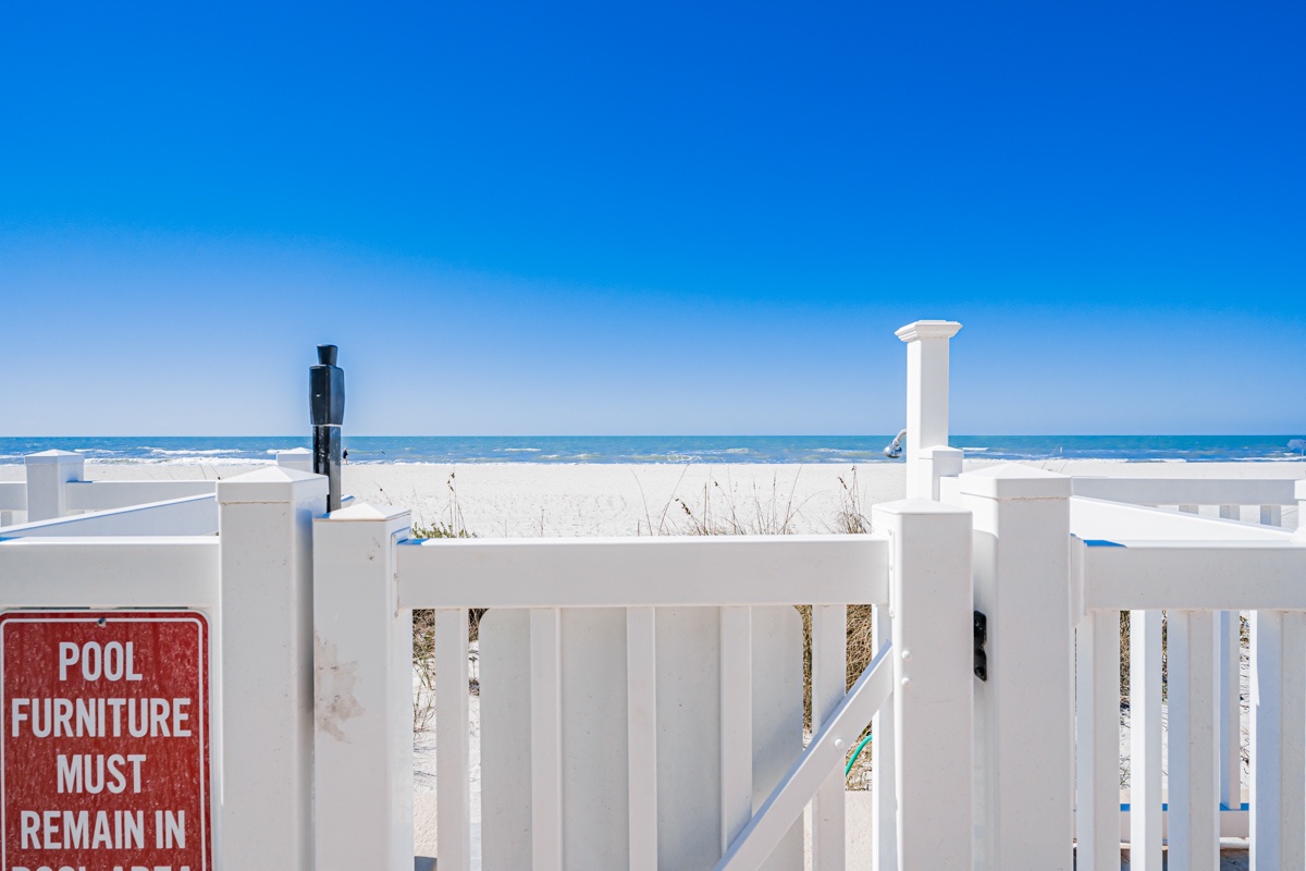 White fencing frames pristine sandy shores and crystal-clear waters under brilliant blue skies at this beachfront property.