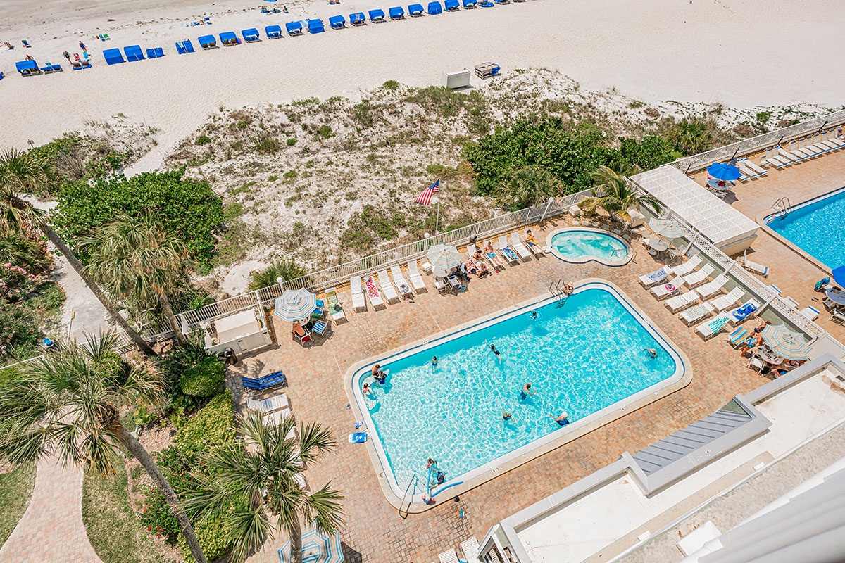 Beachfront property with pools just steps from sandy shores and blue umbrellas.