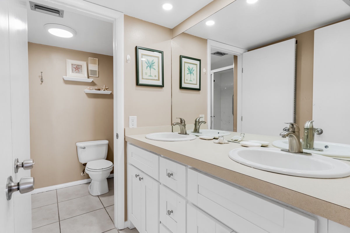 Your spacious bathroom features dual sinks with ample counter space, separate toilet area, and calming coastal artwork to enhance your daily routine.