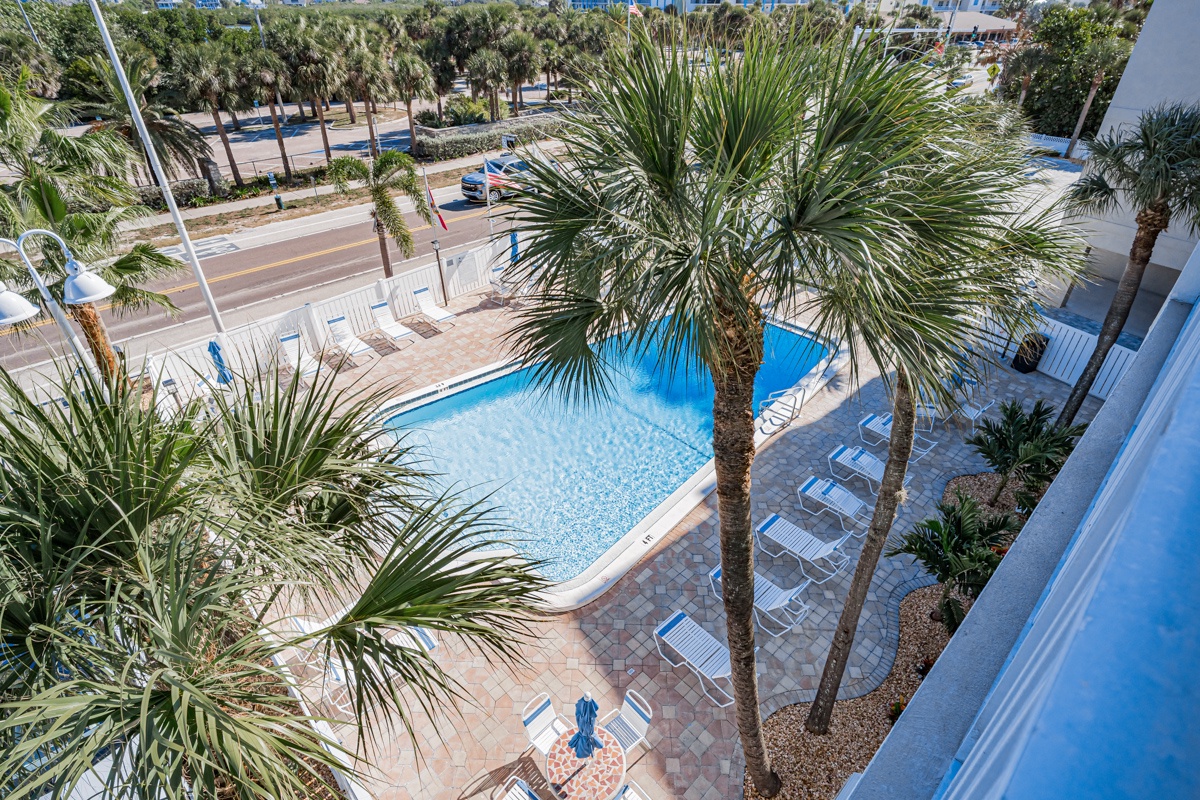 Elevated view showcases the tropical-style pool area surrounded by swaying palm trees and contemporary patio furniture.