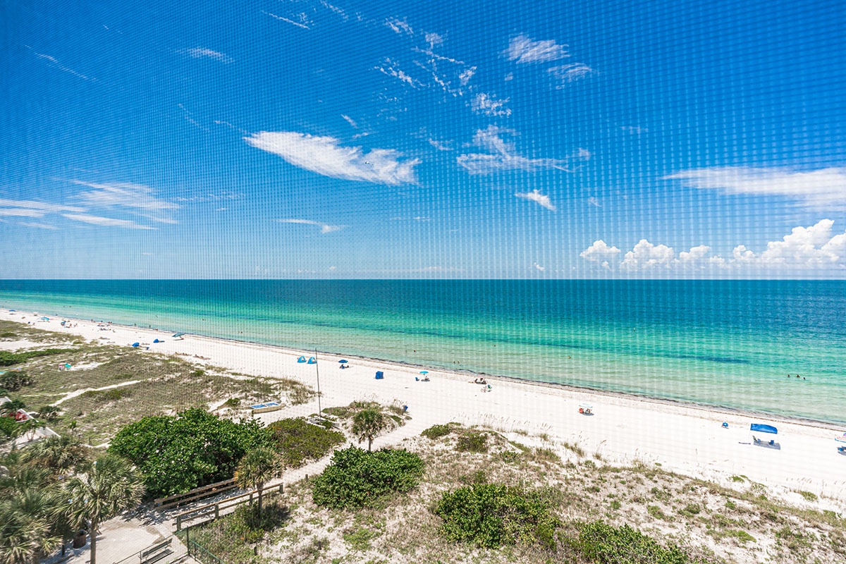 Pristine white sand beach stretches along crystal-clear turquoise waters under bright blue skies with scattered clouds.