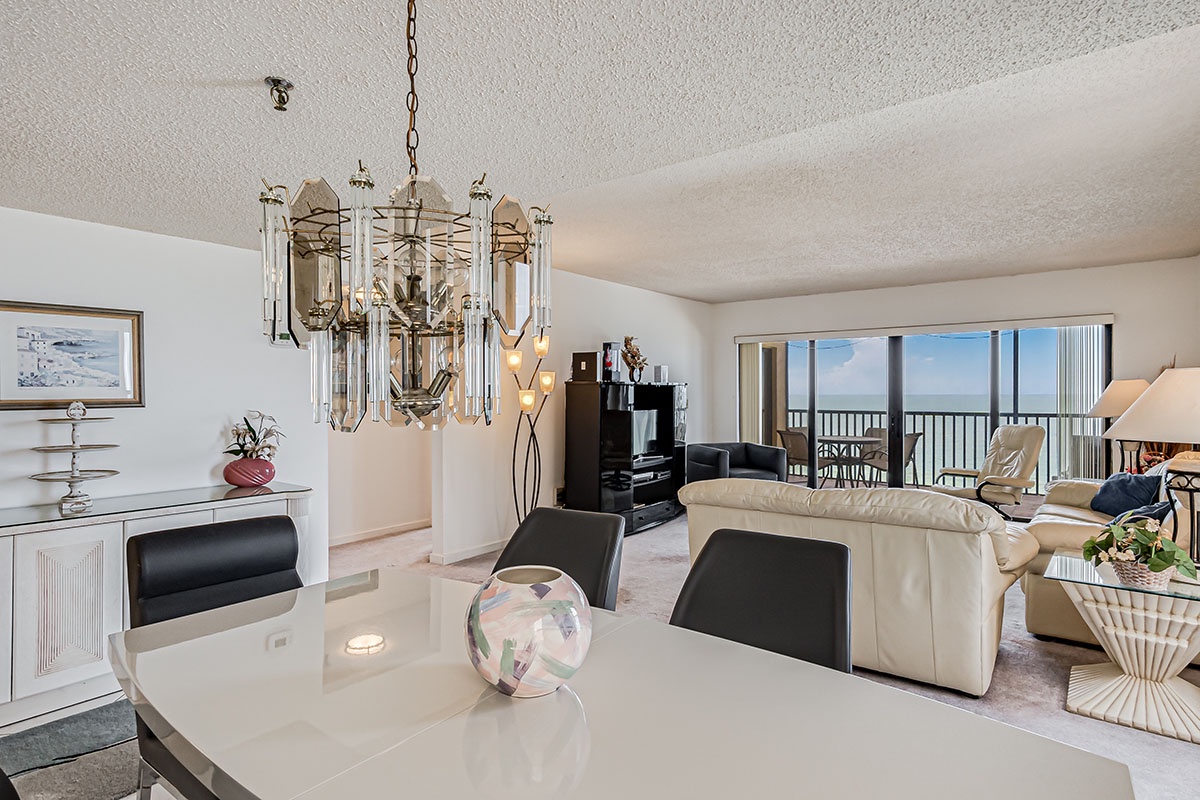 You'll love this elegant open-plan space where a crystal chandelier sparkles above your dining table while ocean views stretch beyond the balcony.
