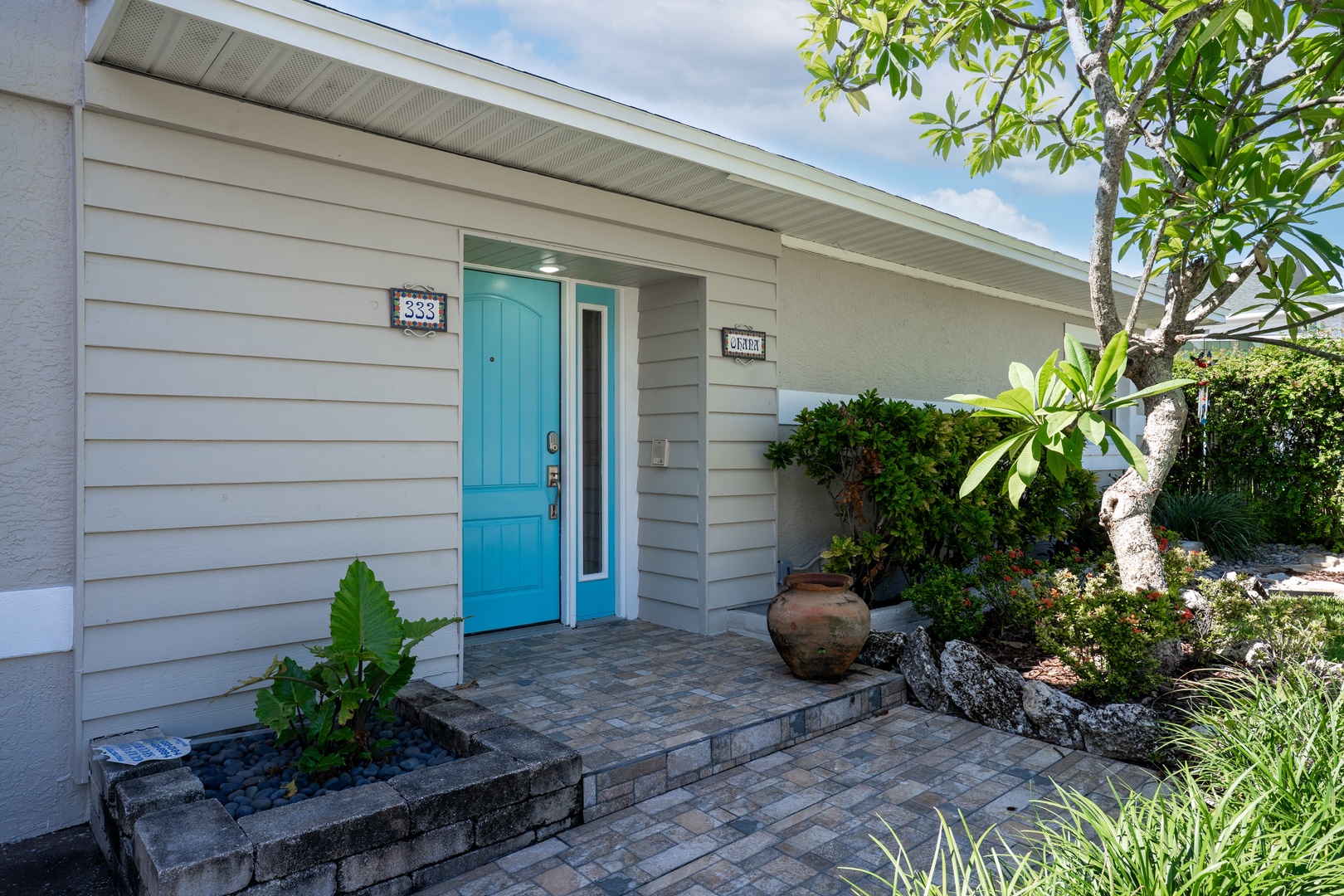 Charming entrance welcomes you with tropical landscaping and a bright turquoise door leading to your coastal retreat.