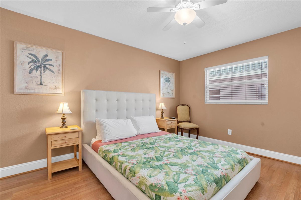 Your cozy retreat features a plush tufted Queen bed dressed in tropical linens, warm lighting, and coastal décor. Unwind beneath the ceiling fan after a day of exploring, surrounded by beachy charm.