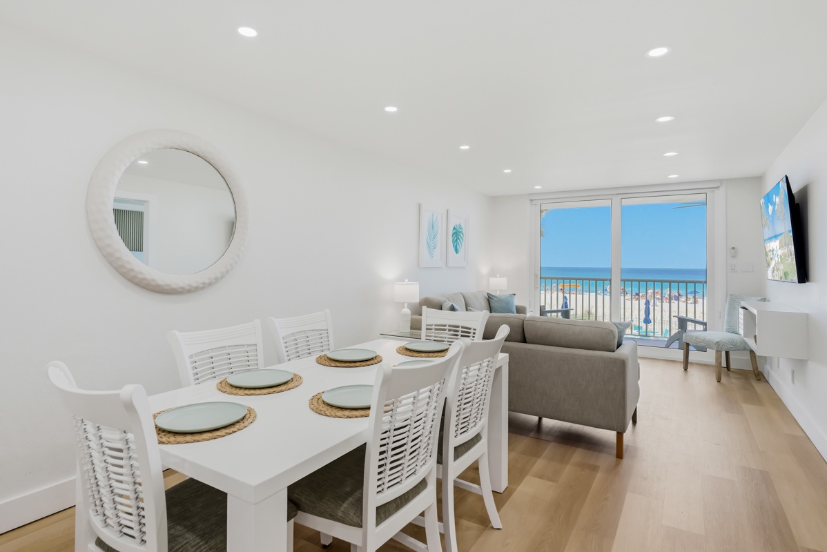 Your bright oceanfront living space features a dining table for six and cozy seating area, all overlooking stunning beach views through floor-to-ceiling windows.
