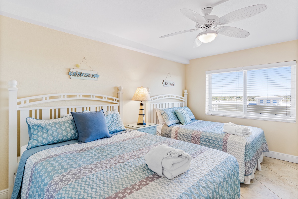 Rest comfortably in your coastal-themed twin bedroom with soft linens, gentle ceiling fan breeze, and bright windows overlooking the area.