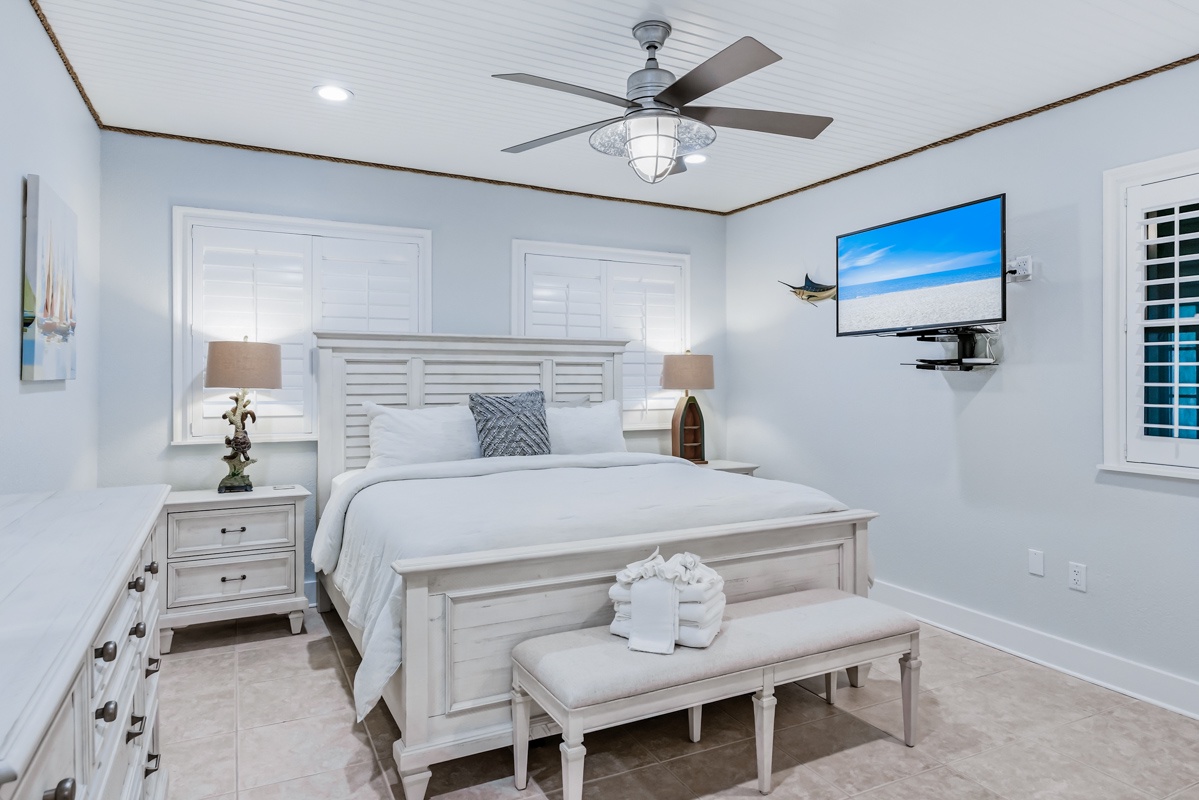 Unwind in your serene coastal bedroom featuring crisp white linens, nautical decor, and a wall-mounted TV for your relaxation.