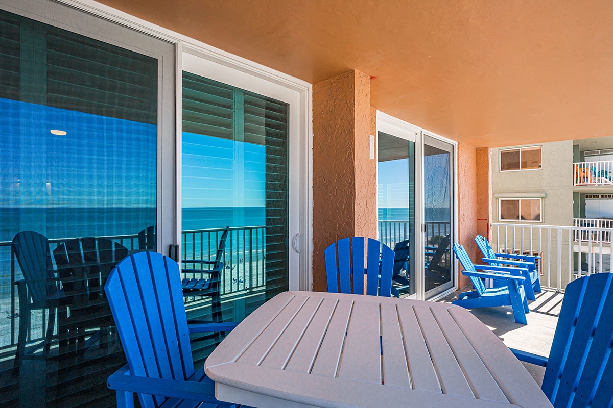 Your private oceanfront balcony features vibrant blue Adirondack chairs and dining table, perfect for morning coffee with endless sea views.
