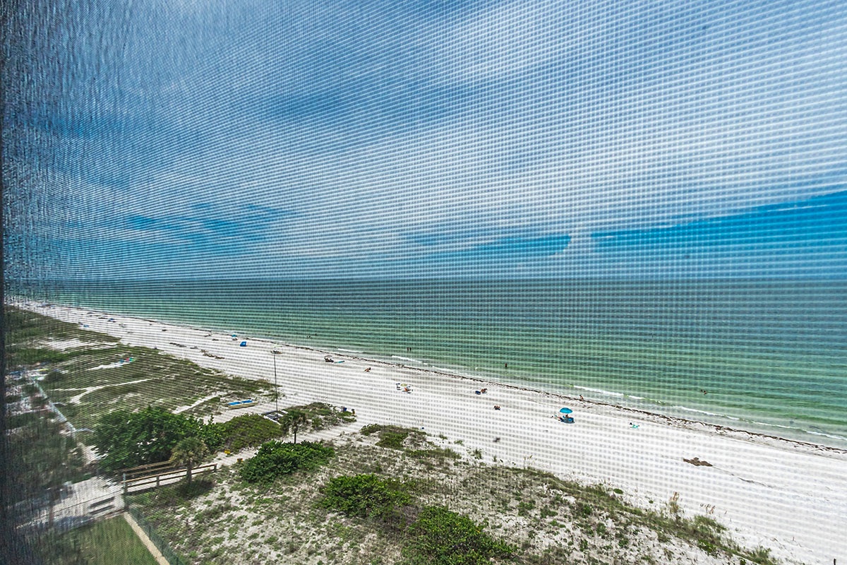 Stunning aerial perspective of pristine white sand beach stretching along turquoise Gulf waters, showcasing the beautiful coastal area surrounding this property.