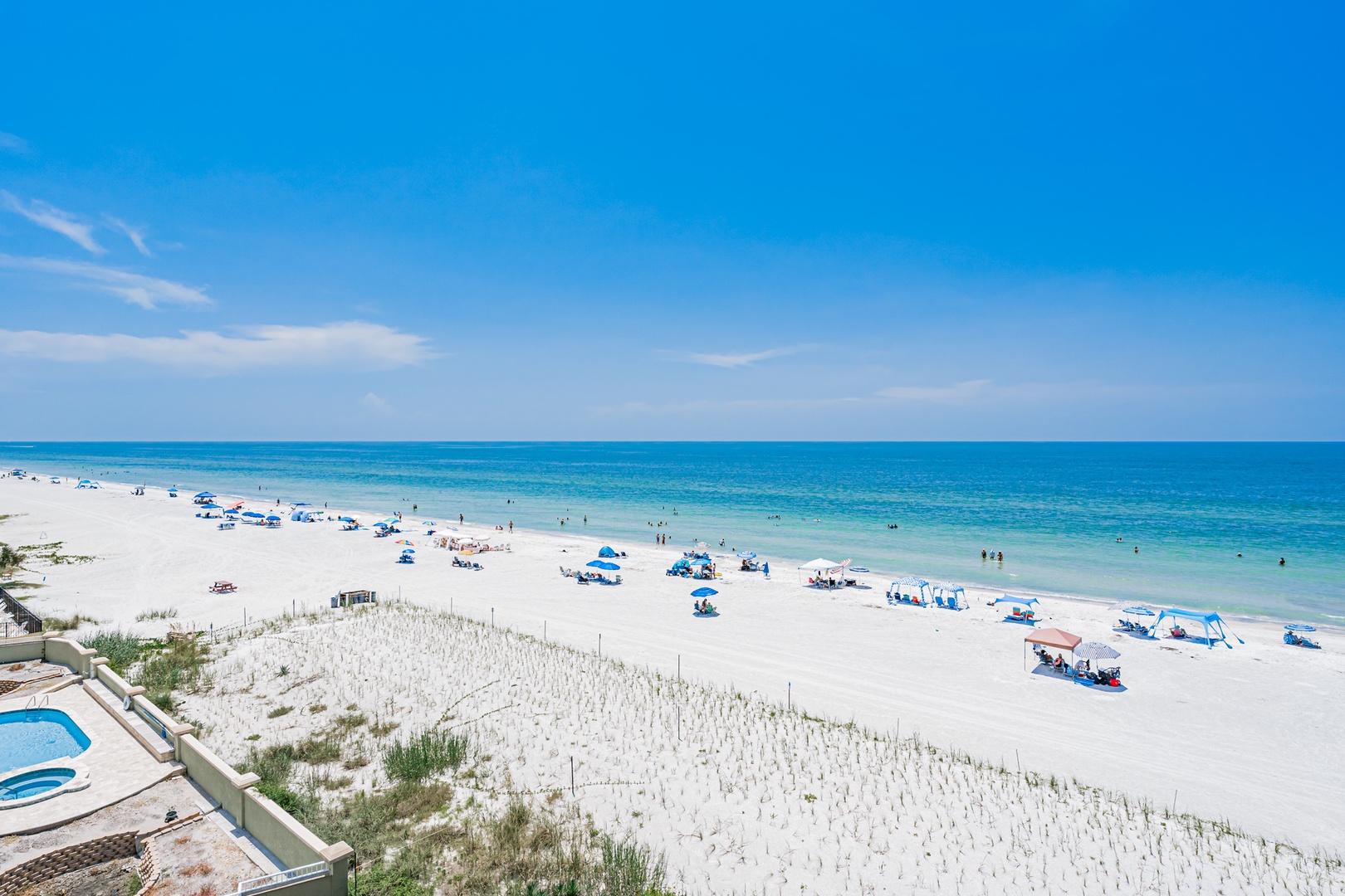 A pristine stretch of white sand beach meets crystal-clear turquoise waters, with a swimming pool visible in the surrounding area for your enjoyment.