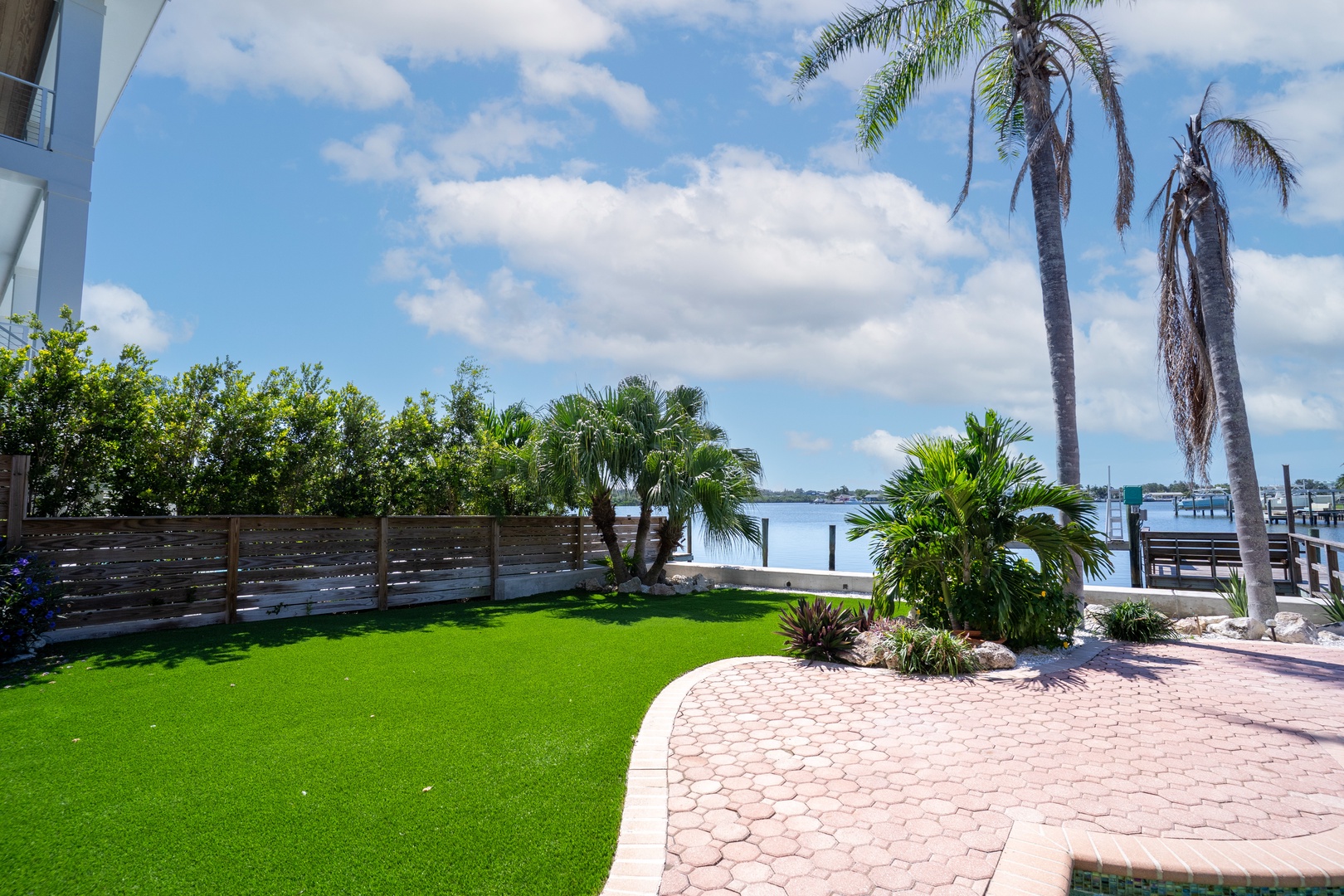 Waterfront paradise featuring tropical palms, pristine artificial turf, and direct bay access with private dock facilities.