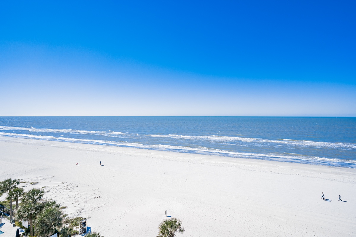 Pristine white sand beach stretches along crystal-clear waters under brilliant blue skies in this stunning coastal location.