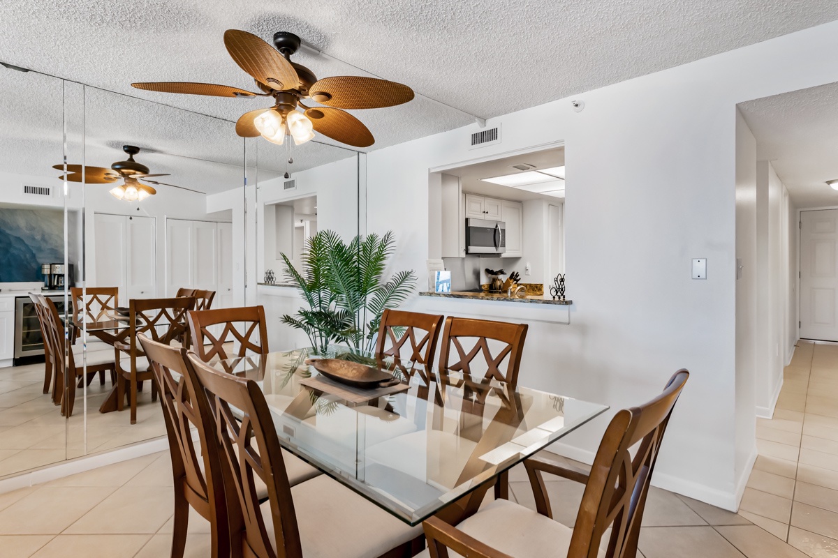 Gather around this elegant dining space where coastal breezes keep you comfortable under your tropical-inspired ceiling fan. The open layout connects you seamlessly to the kitchen, making meal preparation and conversation feel natural and relaxed.