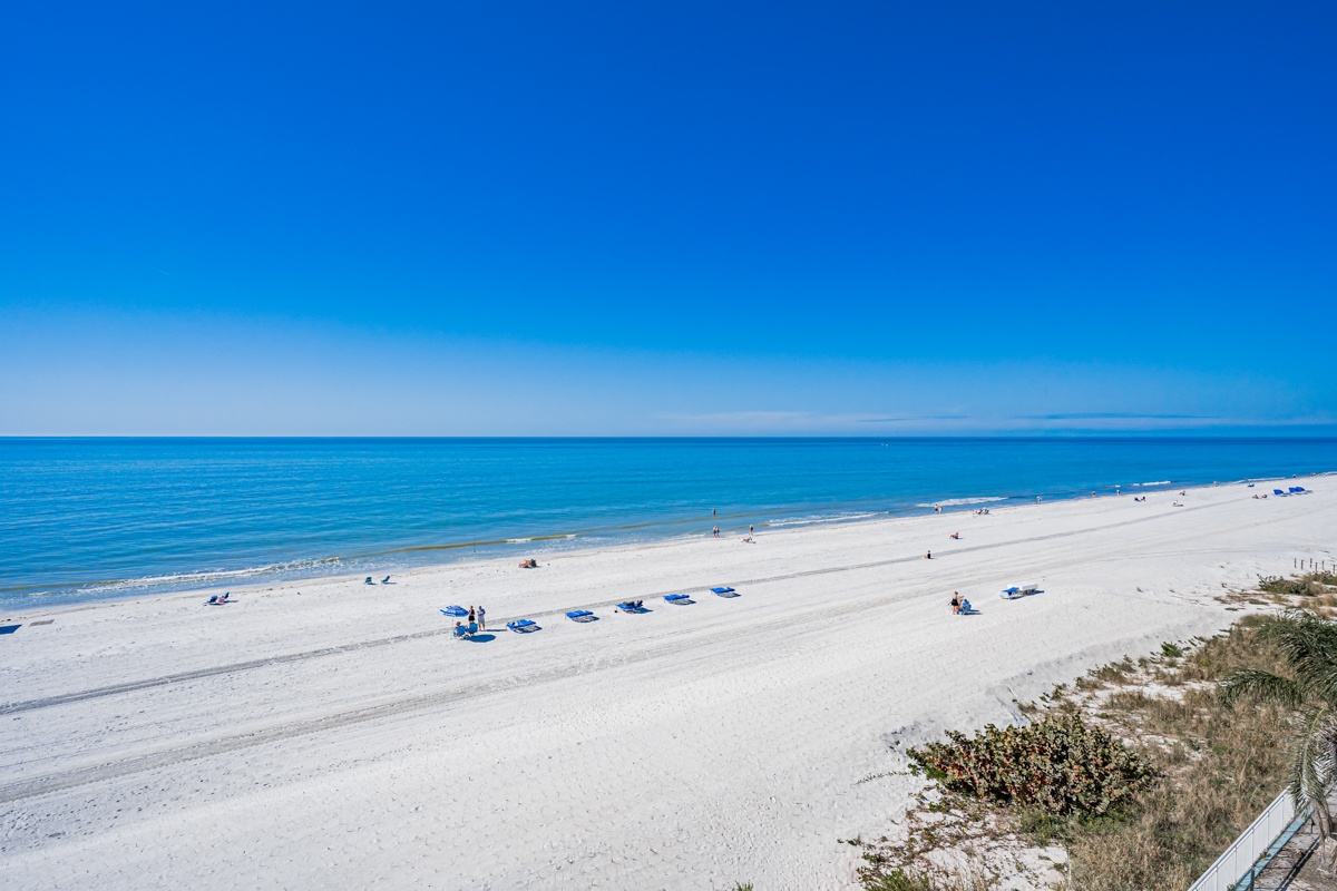 Looking northward, pristine white sand beach stretches along crystal-clear turquoise waters under brilliant blue skies.