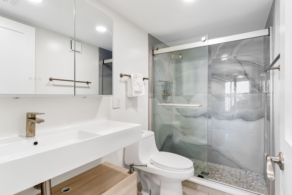 This modern ensuite bathroom offers a sleek retreat with a spacious walk-in shower, clean lines, and thoughtful touches like fluffy towels ready for your stay.