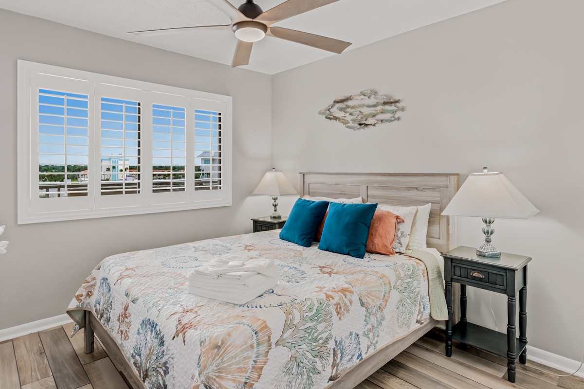 Wake up to bright skies and natural light streaming through plantation shutters. Your restful retreat features a cozy Queen bed, smart TV for entertainment, and a peaceful view beyond the window.