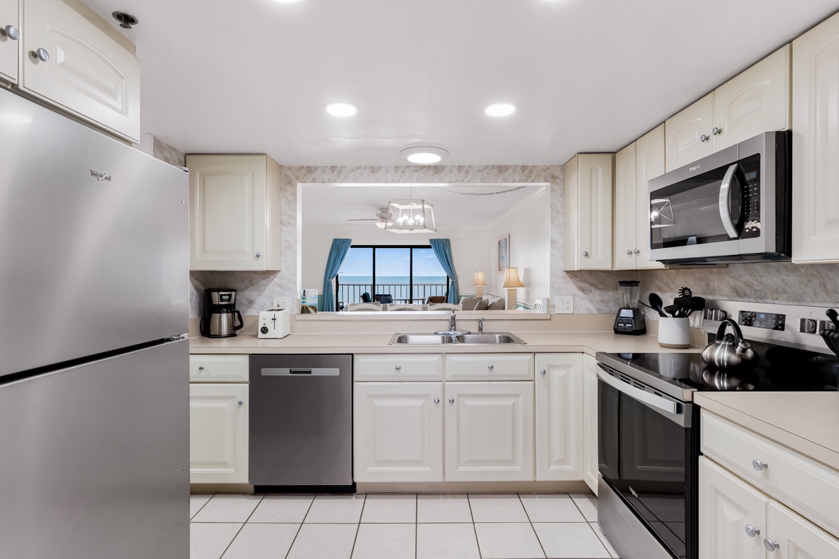 Your fully equipped kitchen features modern appliances and bright white cabinetry, with scenic ocean views beckoning through the living area.