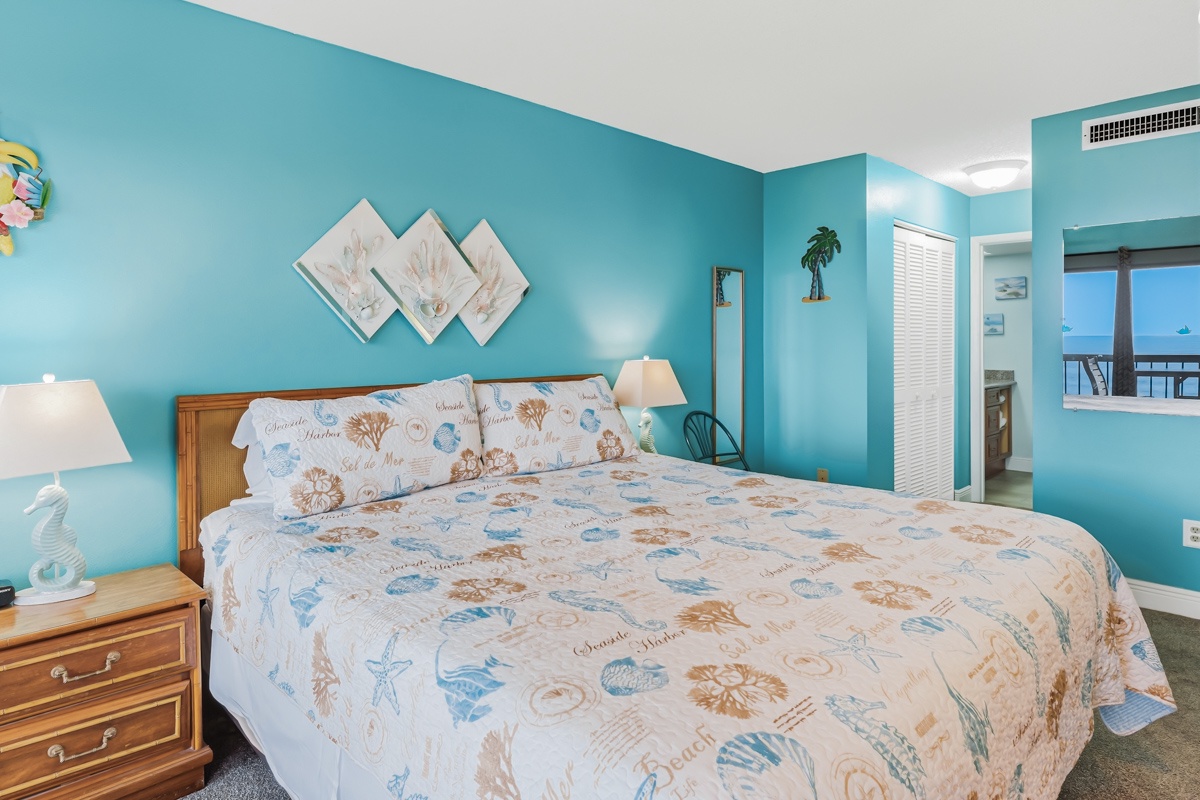 Unwind in your serene coastal bedroom with soothing turquoise walls, beach-themed decor, and a peek of the ocean from your private balcony awaiting.